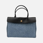 Load image into Gallery viewer, A Chanel handbag featuring a blue denim body, a black leather top flap and handles, and a gold-tone interlocking CC logo on the front, set against a plain light gray background.