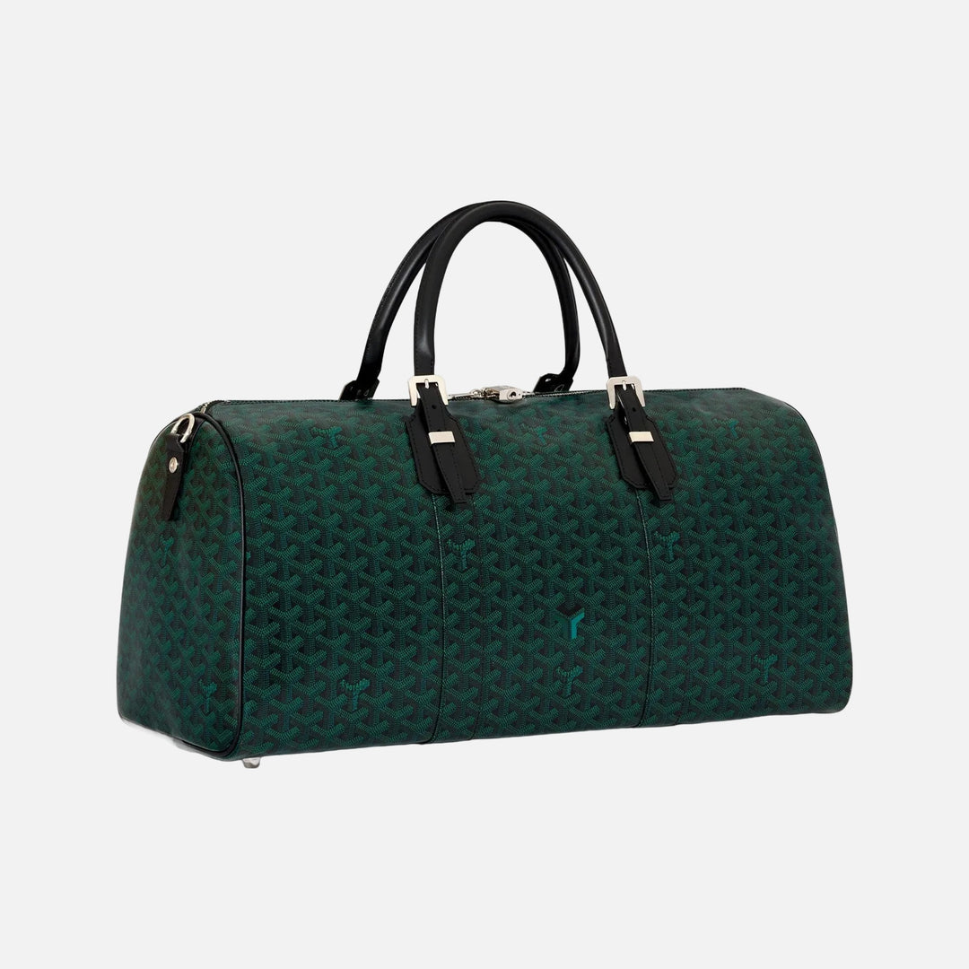 A dark green Goyardine monogram duffel bag with black leather handles and silver-tone hardware, photographed on a clean off-white background.